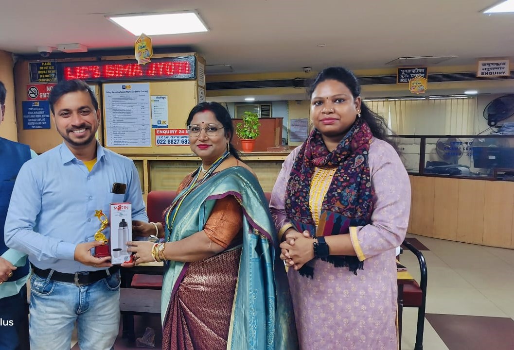 person writing in a notebook beside by an iPad, laptop, printed photos, spectacles, and a cup of coffee on a saucer